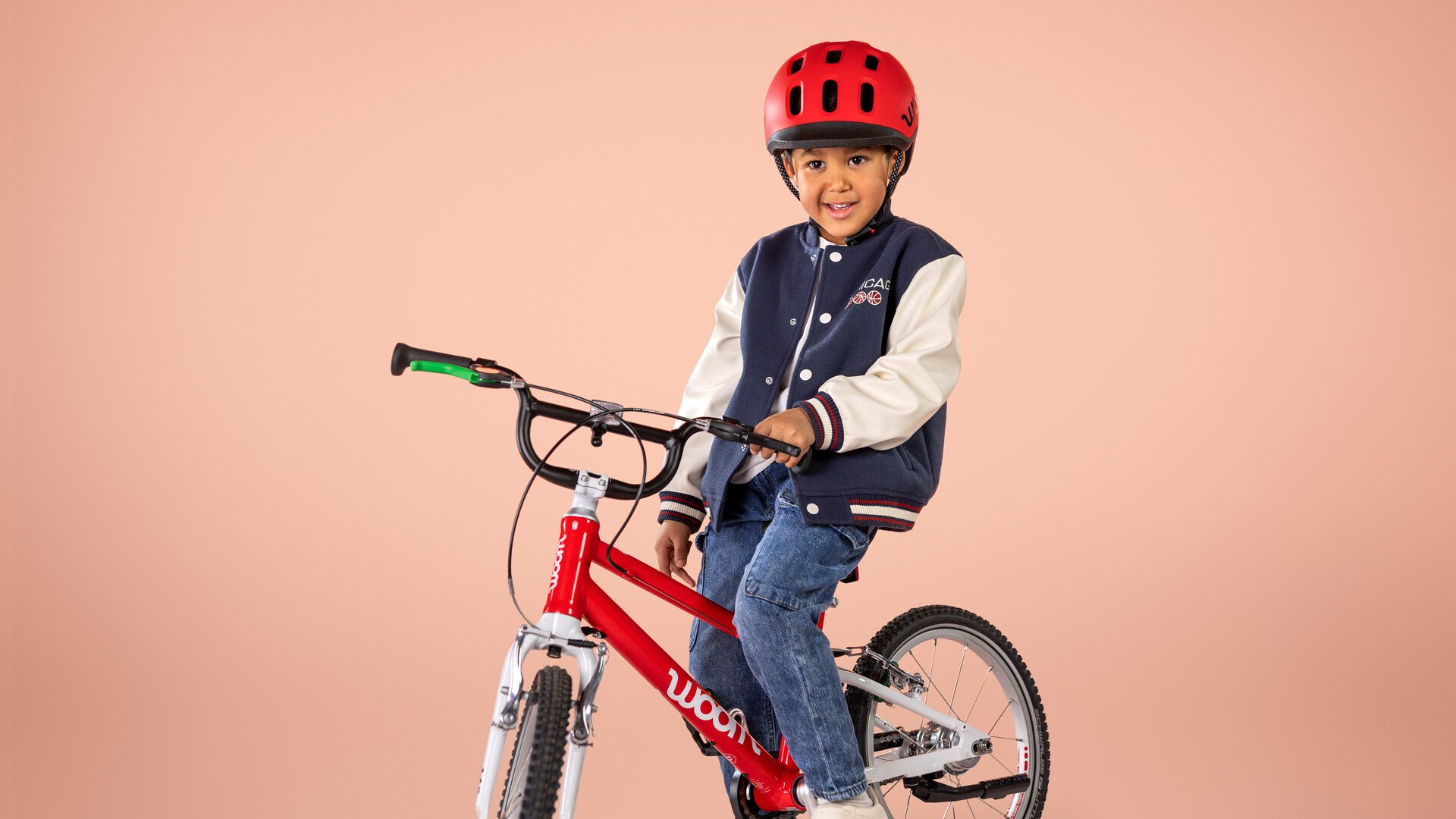 Ein Kind mit rotem READY Helm sitzt auf einem roten Fahrrad mit BMX-Lenker der Marke woom.
