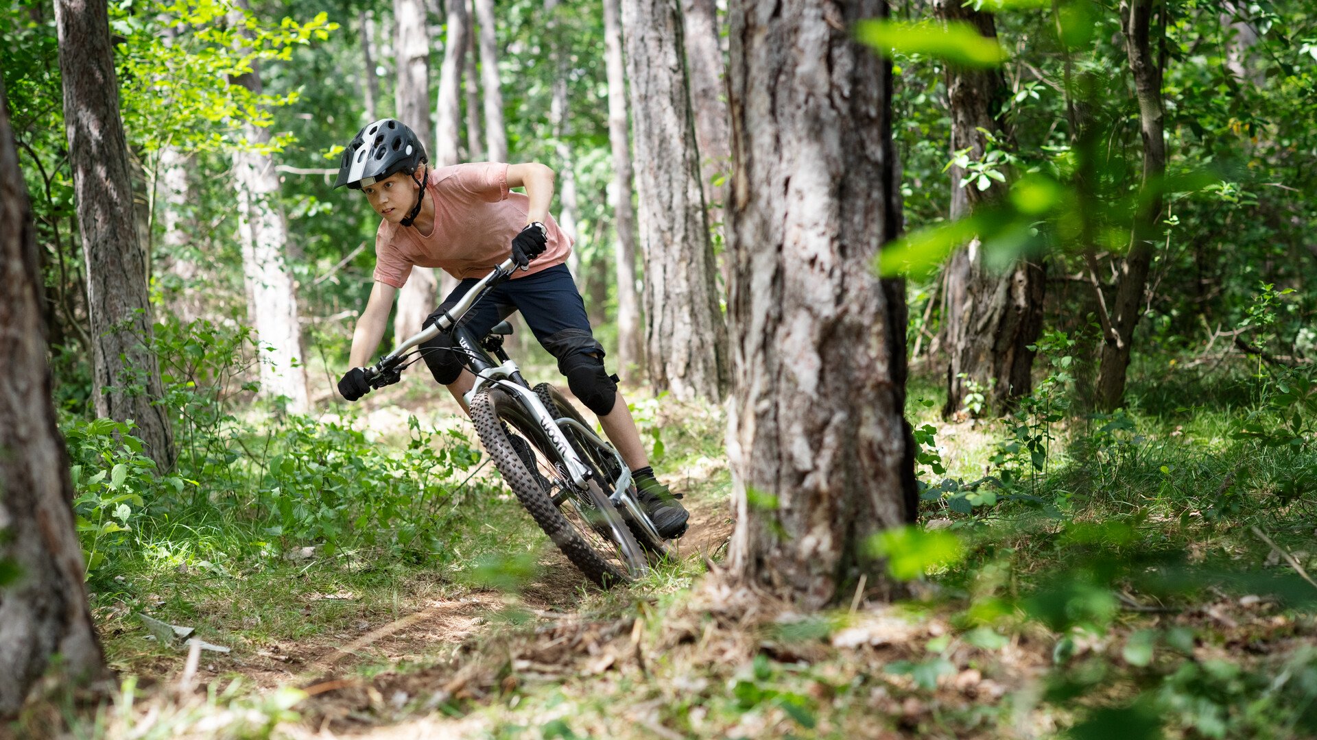 Kind mit Fahrradhelm fährt mit einem schwarzen woom OFF AIR Mountainbike rasant durch eine Trail-Kurve.