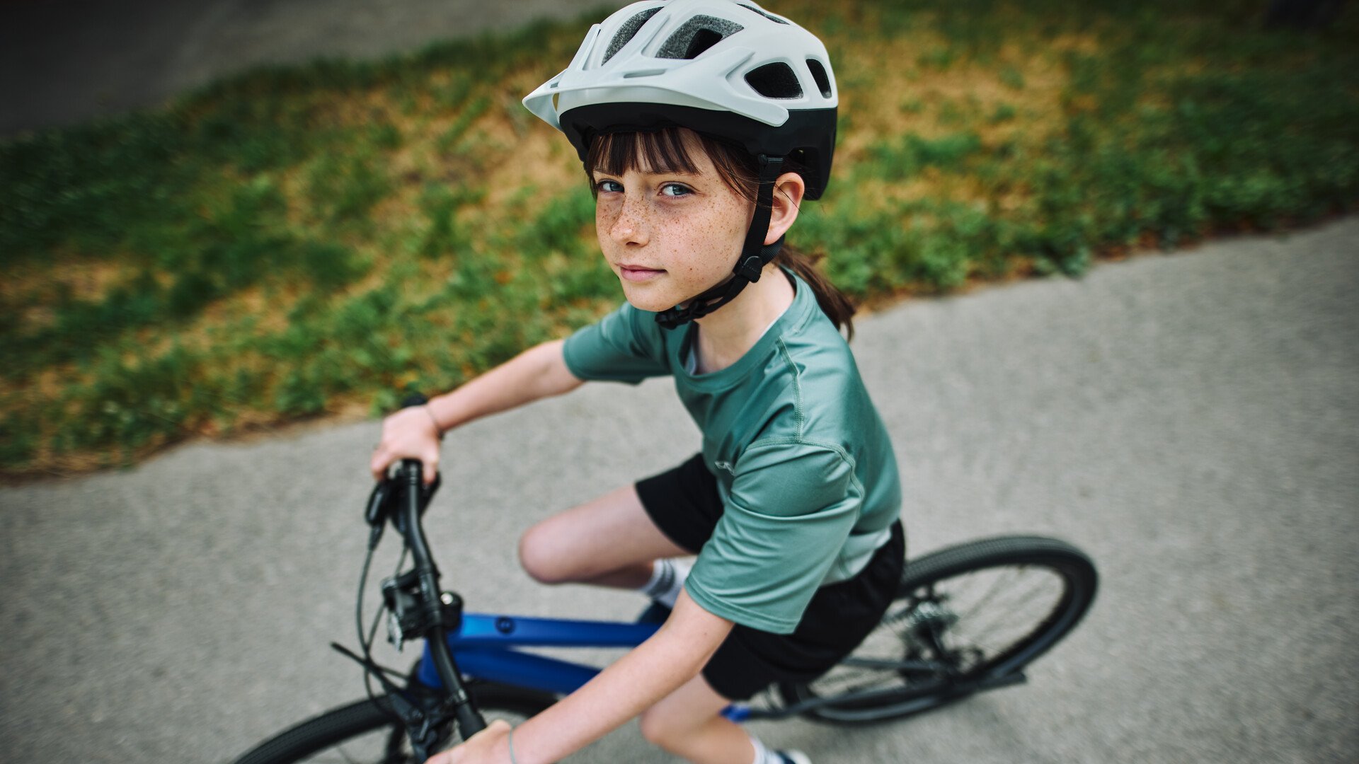 Kind mit Fahrradhelm auf dem Kopf sitzt auf einem woom EXPLORE Fahrrad und blickt nach oben in die Kamera.