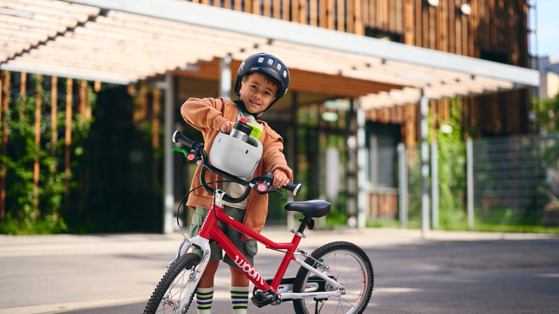 Junge mit READY Helm auf dem Kopf nimmt einen grauen POP Fahrradkorb von seinem Radlenker.