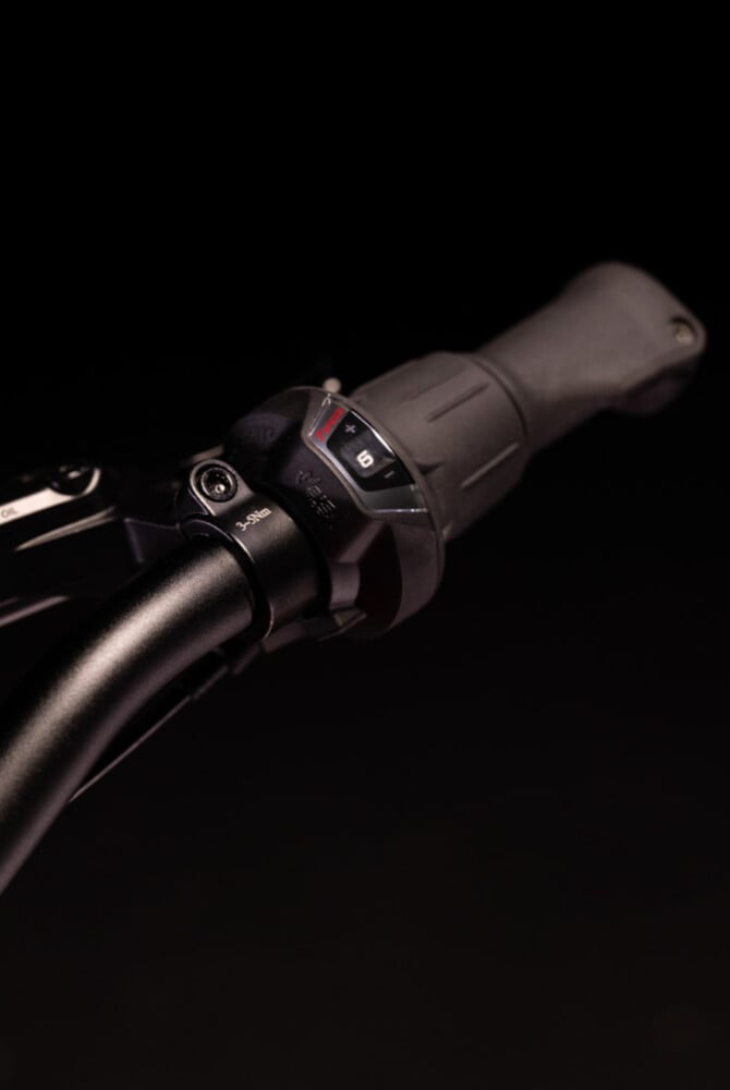 Nahaufnahme des schwarzen woom EXPLORE Lenkers samt schwarzem Shimano Drehschaltgriff mit Ganganzeige.